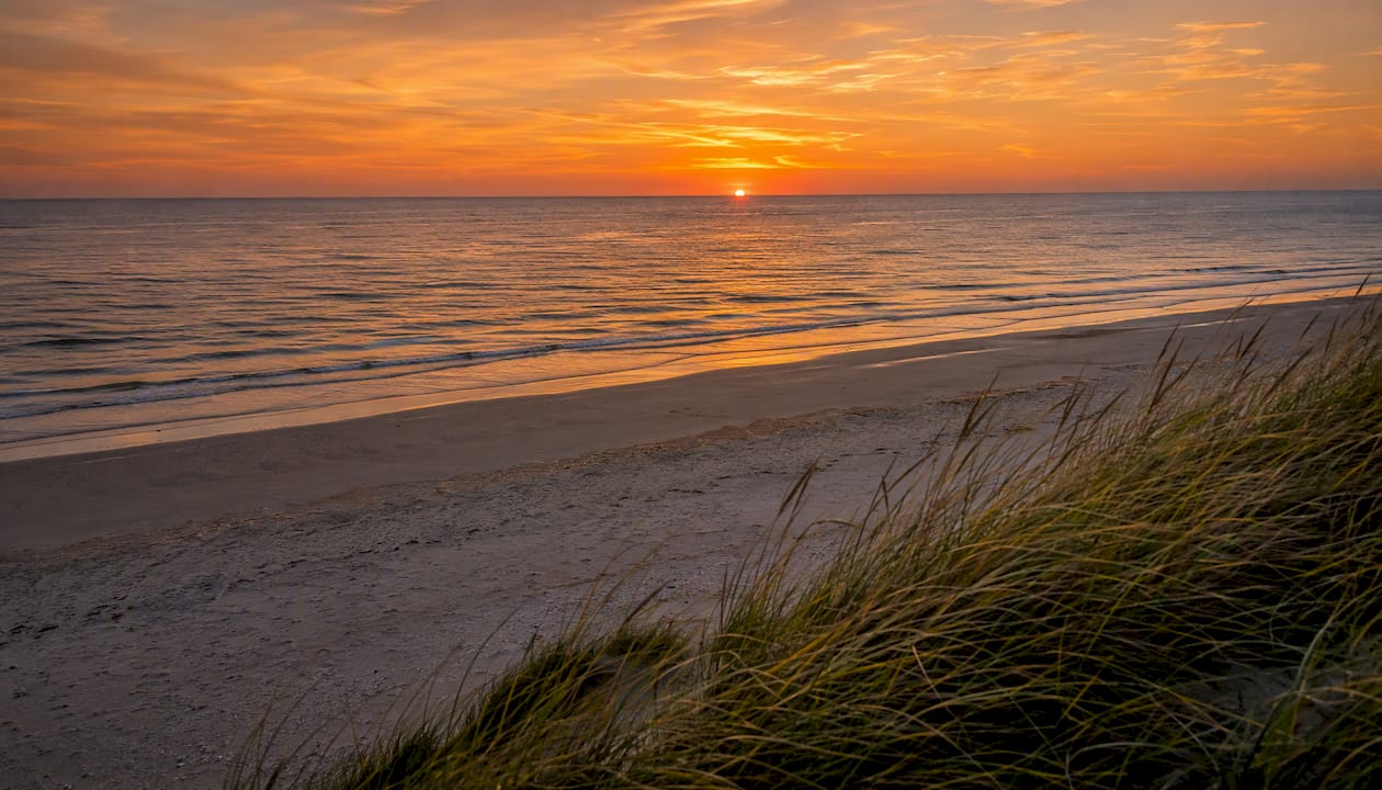 De zon gaat langzaam onder boven het Badstrand bij Hollum, terwijl het licht prachtig weerkaatst op de golven.